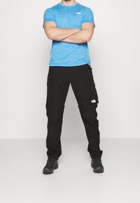 Ljusblå kortärmad skjorta med en logotyp, ihop med svarta cargo-byxor med sidofickor. Svarta skor kompletterar outfiten.