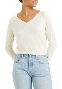 Pull à col en V manches longues de couleur crème, fabriqué en matériau doux, associé à un jean bleu clair taille haute.