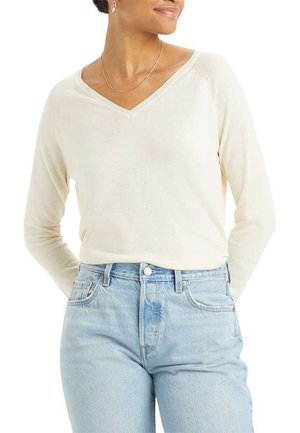 Cream-colored long-sleeve V-neck sweater, made of soft material, paired with high-waisted light blue jeans.