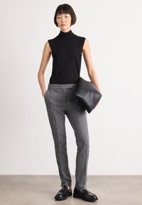 Svart ermeløs høyhalset topp, grå herringbone bukser og svart lær clutch. Modellen har på seg svarte loafers, som viser fram en slank silhuett.