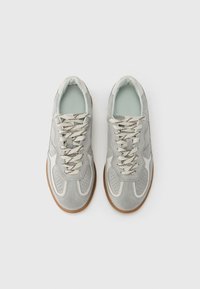 Világosszürke szövetes sportcipők fehér kiemelésekkel és perforált részletekkel. Krémszínű fűzők sötét cikkcakk mintával és gumitalpak.