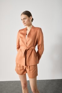 Rust-colored blazer with a belted waist, long sleeves, and a deep V-neckline, paired with matching shorts in a smooth fabric.