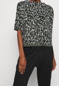 Haut en tricot à manches courtes avec un motif abstrait vert et bleu clair, col rond et coupe décontractée. Associé à un pantalon noir.