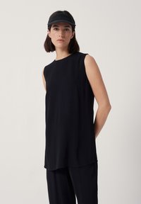 Svart ärmlös topp med rund halsringning, tillverkad av mjukt tyg. Har en rak silhuett och sidoflikar för ökad rörelsefrihet.