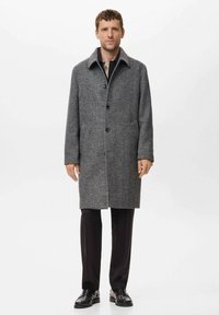 Abrigo de lana gris con collar de solapa, cierre de botones, bolsillos laterales y un diseño de longitud media, combinado con pantalones y zapatos negros.