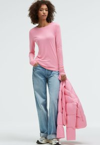 Rosa Langarmshirt, hellblaue weite Jeans und eine gefaltete rosa Pufferjacke. Weicher Stoff mit lockerer Passform und subtilen Nähten.