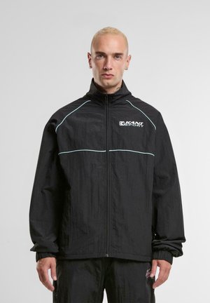 Veste coupe-vent noire avec col montant, fermeture éclair, lignes d'accent bleu clair et poignets élastiques. Présente le logo KANI SPORTS sur la poitrine.