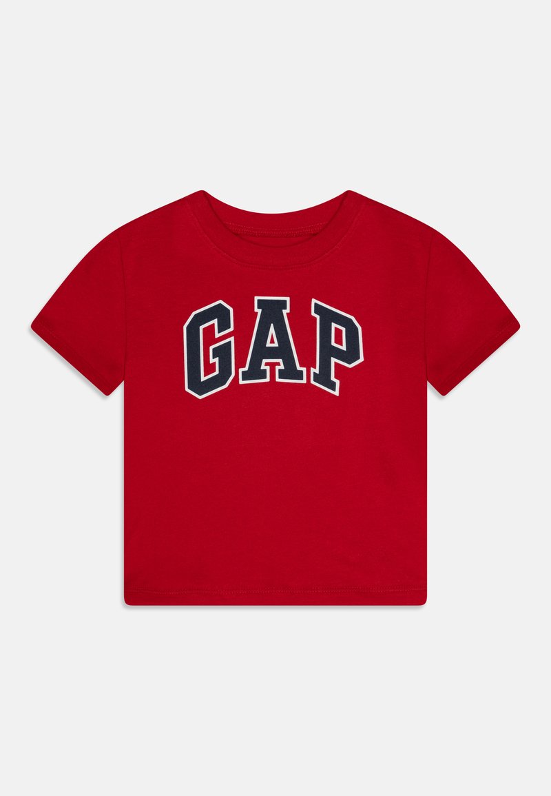 Sarkans kokvilnas t-krekls ar īsām piedurknēm, uz kura krūtīm ir boldā, arku formā izdrukāts tumši zils "GAP" logo.