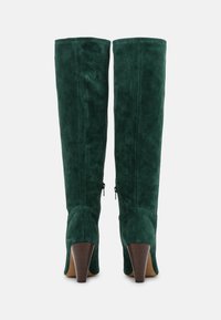 Bottes montantes en daim vert foncé avec talons blocs empilés et fermetures éclair latérales, vues de dos sur fond blanc.