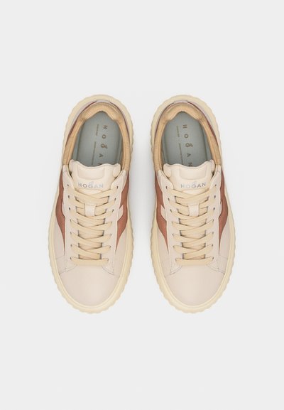 Ζευγάρι δερμάτινων αθλητικών παπουτσιών σε μπεζ και καφέ χρώμα με χοντρές κρεμ σόλες και κορδόνια, απόψε από πάνω, με εμφανές το όνομα της μάρκας "Hogan" στη γλώσσα και στα πέλματα.