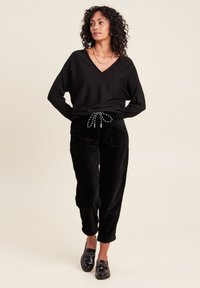 Pull noir oversize à col V associé à un pantalon en velours côtelé noir avec une taille élastique. Des mocassins noirs brillants complètent le look.