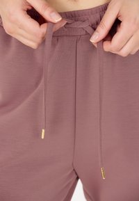 Enigezins taps toelopende, mauve joggingbroek met een trekkoord in de taille. Zachte stof, met gouden aglets op de snoeren en een subtiele textuur.