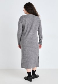 Rochie tricotată gri, cu dungi, de lungime medie, cu mâneci lungi și fante pe lateral. Asortată cu pantofi negri fără toc și sosete negre până la gleznă.