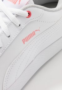 Zapatilla blanca de cuero sintético, con logo Puma rosa, detalles texturizados y cordones blancos con un toque de rosa en las ojeteras.