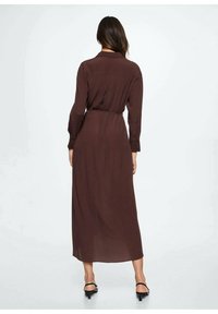 Długa brązowa sukienka z lekkiego materiału, z kołnierzykiem, z zapięciem na guziki z tyłu i ściągniętą talią. Teksturowana o gładkim wykończeniu.