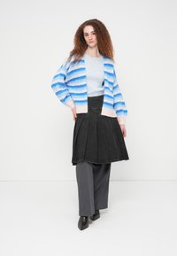 Ριγέ ζακέτα σε ανοιχτό μπλε και ροζ, συνδυασμένη με πλισέ μαύρη τζην φούστα και γκρι παντελόνι με φαρδιά μπατζάκια, συνοδευόμενη από σκοτεινά μποτάκια με τακούνι.