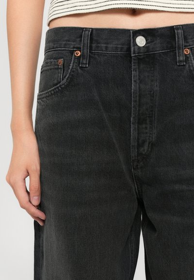 Jean en denim noir à taille haute, avec des éléments en métal cuivré, un design à cinq poches et des coutures apparentes.