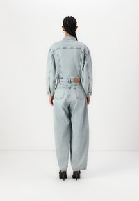 Lys blå denim jumpsuit med en avslappet passform, med lange ermer, belte i midjen og et rektangulært baklomme-design.