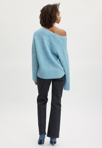 Svetlo modrý oversized sveter s rebrovanou textúrou, s designom odkrytých ramien, skombinovaný s tmavými denimovými nohavicami a modrými vysokými topánkami.