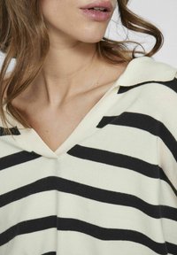 Maglione a righe con scollatura a V, realizzato in morbido tessuto a maglia color crema con audaci strisce orizzontali nere. Dettagli del colletto accentuati.