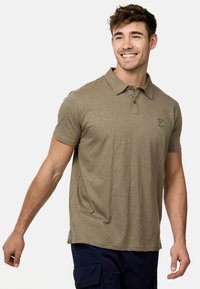 Polo olive vert à manches courtes, avec une patte de boutonnage à deux boutons et un logo sur la poitrine gauche. Fabriqué en tissu texturé avec une coupe décontractée.