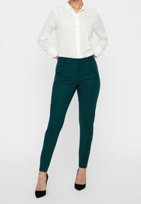 Miętowe dopasowane spodnie z bocznymi kieszeniami, połączone z białą koszulą z guzikami. Gładki materiał o lekko połyskującej powierzchni. Czarne szpilki.