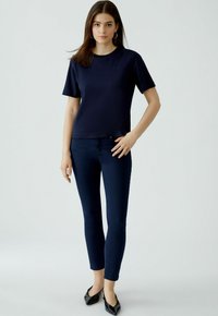 Marineblauwe t-shirt met korte mouwen en een ronde hals, gecombineerd met donkere skinny jeans. Zwarte puntige ballerina's maken de outfit compleet. Eenvoudig en aansluitend ontwerp.