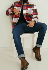 Rød og sort ternet flannel skjorte med hvide detaljer, mørke jeans og brune ankelstøvler. Har opsmøgede ærmer og en slim fit.