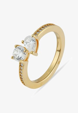 Anello d'oro con due grandi gemme trasparenti—una rotonda, una a forma di pera—e pietre più piccole incastonate lungo i bordi della fascia.