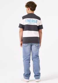 Camiseta de rayas en gris y blanco con texto azul "ENERGY" en la parte posterior, combinada con jeans de denim azul claro y zapatillas blancas. Ajuste casual.