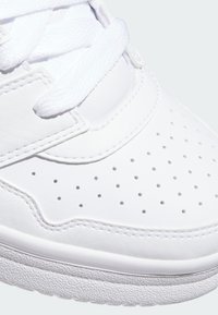 Vit sportig sneaker med en slät läderöverdel, perforerat mönster för andningsförmåga, runda snören och strukturerad gummisula.