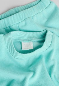 Vaalean mintunvihreä vauvanvaatesetti, jossa on resorikaulus ja pehmeä kangas. Sisältää samanväriset housut, joissa on joustava vyötärönauha.