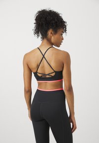 Top atlético negro con tirantes entrecruzados y acentos en rosa, combinado con leggings negros de tiro alto que presentan una textura suave y un diseño ceñido.