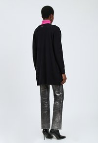 Zwarte lange mouw trui met een roze kraag, gecombineerd met glanzende zilveren rechte broek en zwarte haklaarzen. Eenvoudig ontwerp met minimale accenten.
