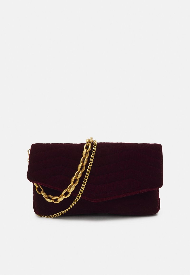 Pochette en velours violet foncé avec un rabat et deux bandoulières chaînes dorées, l'une épaisse et l'autre fine, sur un fond clair uni.