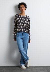 Svetr s dlouhým rukávem a geometrickým vzorem v tmavě šedé a světlé béžové, zkombinovaný se světlými modrými džíny s vysokým pasem a bílými teniskami.