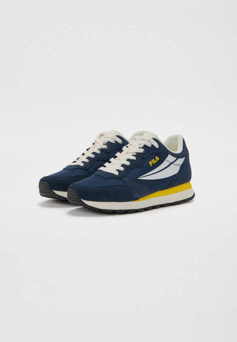 Scarpe sportive blu navy con lacci e dettagli color crema. Presentano un logo bianco, una striscia gialla sul suola e una suola in gomma per una migliore aderenza. Pannelli in suede testurizzato.