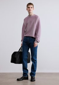 Ανοιχτό μωβ πλεκτό πουλόβερ με ριμπ γιακά, συνδυασμένο με μπλε τζιν παντελόνι. Το μοντέλο κρατάει μια μαύρη τσάντα και φοράει μαύρα παπούτσια. Απλό και μοντέρνο.