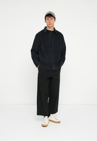 Black checkered button-up shirt, black wide-leg trousers, and cream sneakers with light brown soles; casual outfit with a structured design.