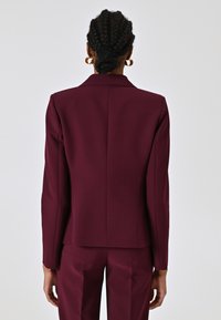 Bordeaux gesneden blazer met lange mouwen, uitgesneden kraag en strakke lijnen. Gladde textuur, split aan de achterkant, gecombineerd met bijpassende broek.
