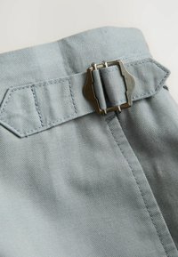 Hellblaues Denimgewebe mit einem metallenen Schnallenverschluss an der Taille, sichtbaren Nähten und strukturierten Oberflächen.