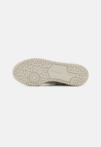 Adidas sneaker sole with a textured, light beige rubber, featuring circular patterns and the Adidas logo prominently displayed.