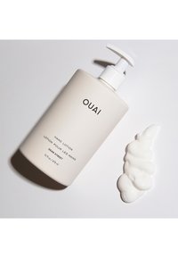 Pumpflaska med OUAI handlotion i en mjuk beige färg, med svart text. En virvel av vit lotion ligger bredvid på en ljus bakgrund.