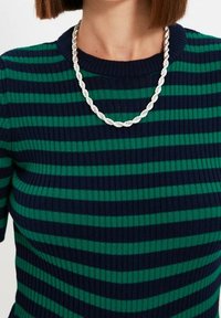 Haut tricoté rayé en bleu marine foncé et vert, présentant une texture côtelée. Orné d'un collier argenté torsadé autour du cou.