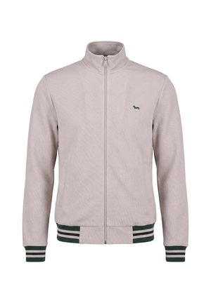 Lysebeige lynlåsjakke med opretstående krave, grønne og hvide stribede ærmeafslutninger og kant samt lille grønt hundelogo på brystet.