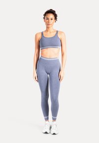 Blaues athletisches Crop-Top und hoch taillierte Leggings mit strukturiertem Stoff und gestreiften Akzenten, kombiniert mit weißen Turnschuhen, vor einem neutralen Hintergrund präsentiert.
