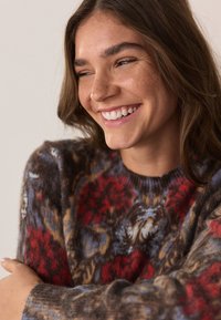 Džemper na pletenje s šarenim cvjetnim uzorkom u crvenim, plavim i smeđim nijansama, s okruglim izrezom i mekanim, teksturiranim materijalom.