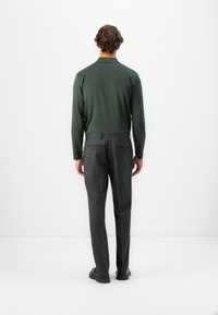 Forest green long-sleeve shirt paired with grey pinstriped trousers. The outfit features a fitted design and soft texture. Black shoes complete the look.