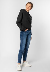 Zwarte hoodie met een voorzak, gecombineerd met blauwe slim-fit jeans en witte sneakers. Soepele texturen en een casual ontwerp.
