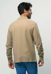 Pika kauakäistehall polo särk mugava tekstuuriga, millel on krae ja soonikkoes varrukad, koos siniste teksadega.